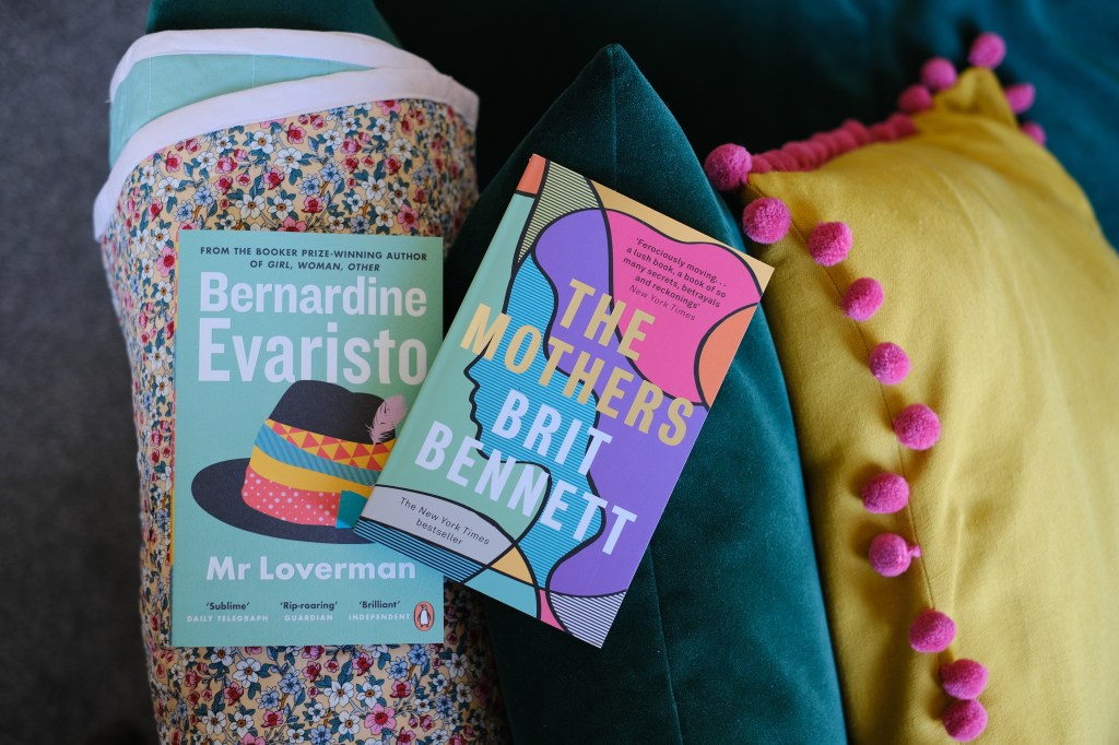 Two books on a green sofa. The books are Mr Loverman by Bernadine Evaristo and The Mothers by Brit Bennett. 